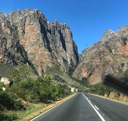 7 days Hidden Local Gems Two-lane road winds through a canyon with tall rock cliffs on both sides under a clear blue sky.