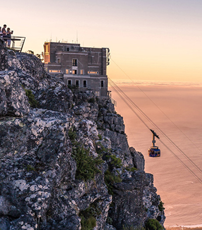 How Many Days Are Enough for Cape Town People stand on a rocky cliff edge watching a sunset as a cable car glides toward the sea beside a weathered building on the cliff. (informative)