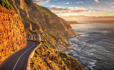 If You Only Have Two Days in Cape Town Day 2 Winding road along towering orange cliffs beside a rocky coastline at sunset.